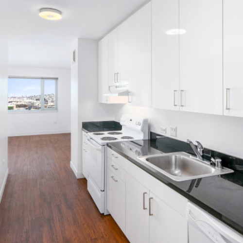 Studios in San Francisco, CA - Trinity Place at 1190 - A Kitchen with White Cabinets, Black Granite Countertops, a Sink, Electric Stove, Dishwasher, and Refrigerator.
